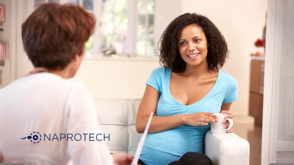 Mujer embarazada conversando con una profesional de salud en consulta sobre fertilidad y métodos naturales, representando el enfoque ético de Naprotech.