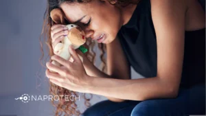Mujer llorando mientras sostiene un peluche, simbolizando el dolor emocional ante la dificultad para quedar embarazada, con el logo de Naprotech al fondo.
