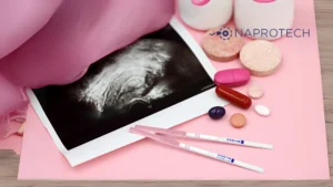Fotografía de una ecografía sobre fondo rosado junto a pruebas de embarazo, cápsulas y tabletas de diferentes colores. En la parte superior derecha se observa el logo de Naprotech